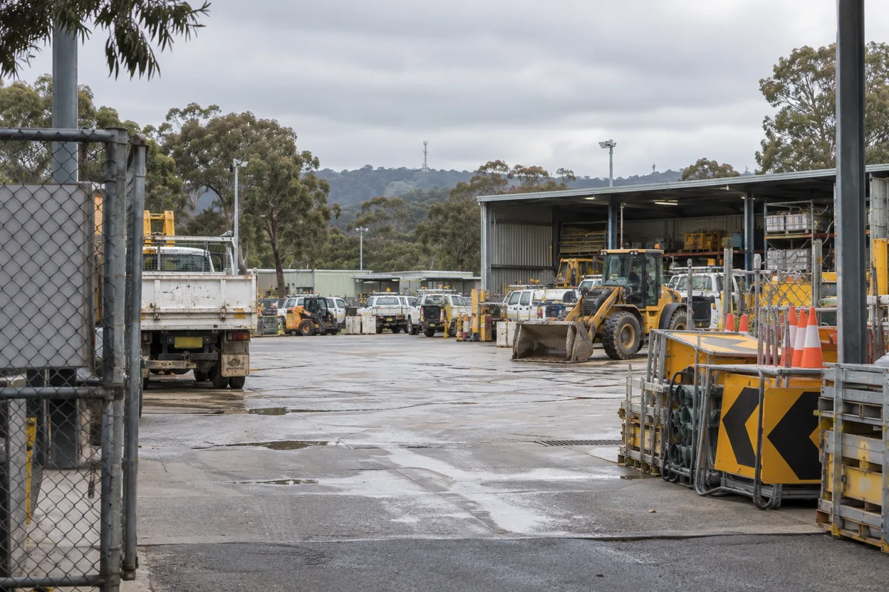 A council depot yard seen from the gate, mobile plant and a stack of road signage visible, the kind of site a works team runs alongside dozens more