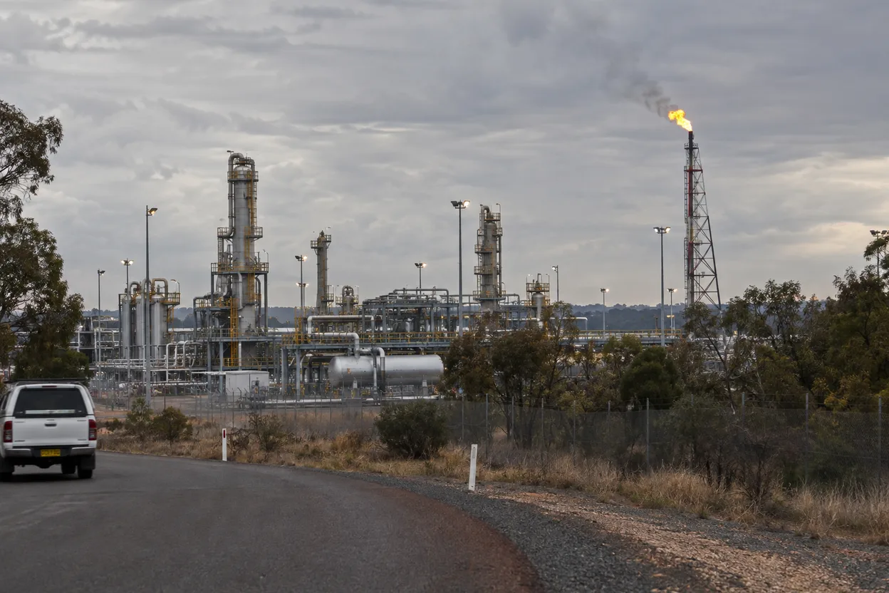 A gas plant flare stack and pipework seen from the perimeter road, the kind of site an oil and gas operator runs
